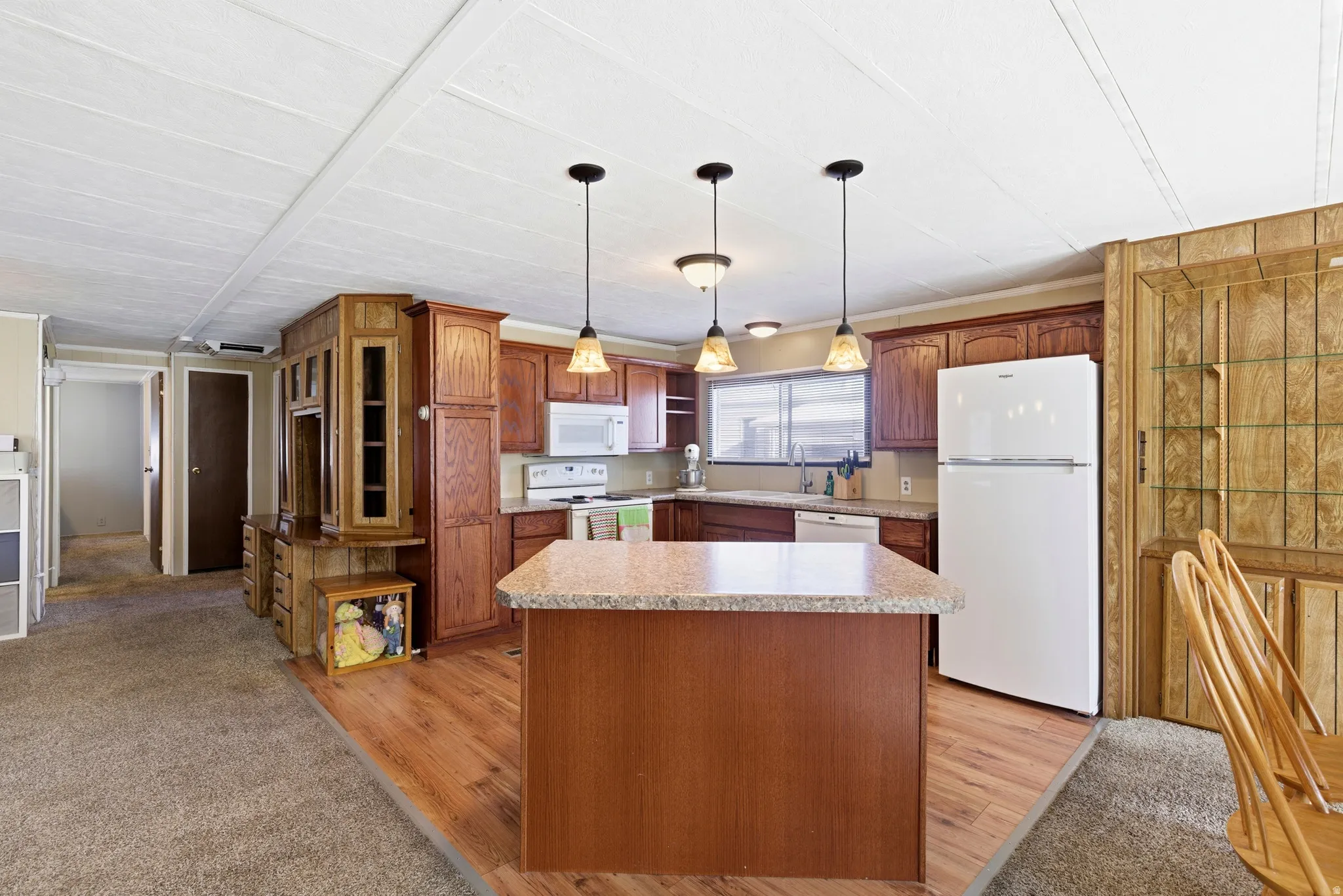 Kitchen with white appliances, pendant lighting, light countertops, brown cabinetry, and a kitchen island