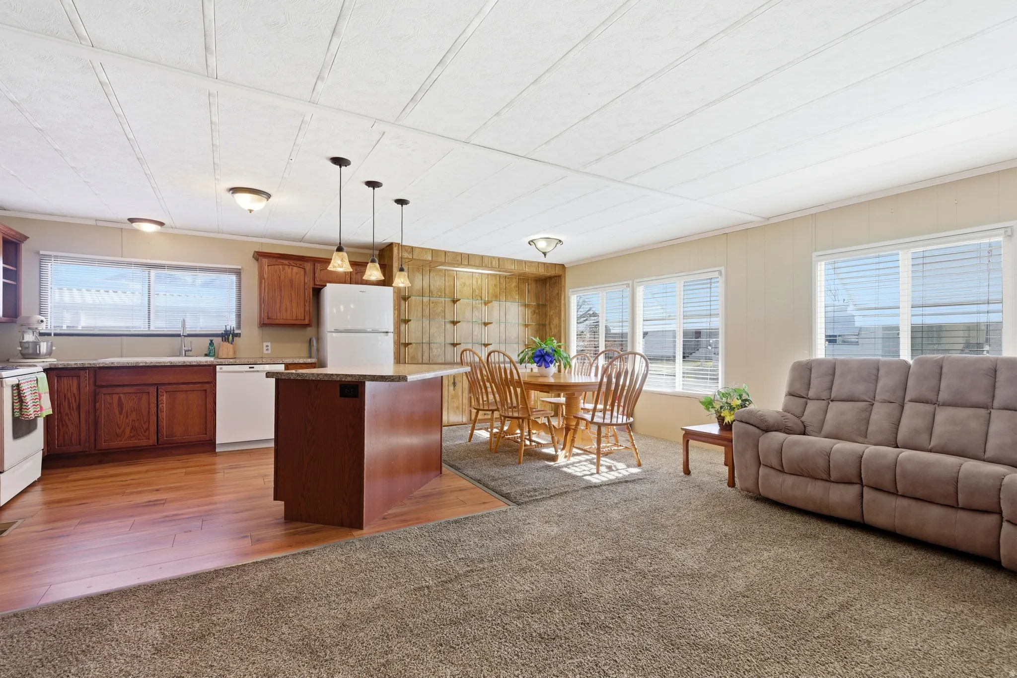 Kitchen with hanging light fixtures, white appliances, brown cabinets, a center island, and open floor plan