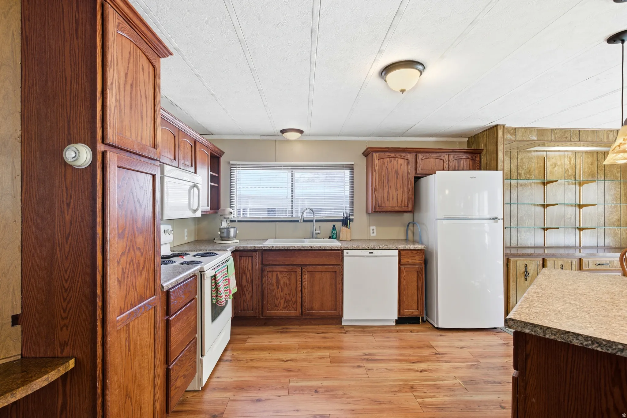 Kitchen featuring white appliances, brown cabinetry, light wood-style flooring, pendant lighting, and light countertops