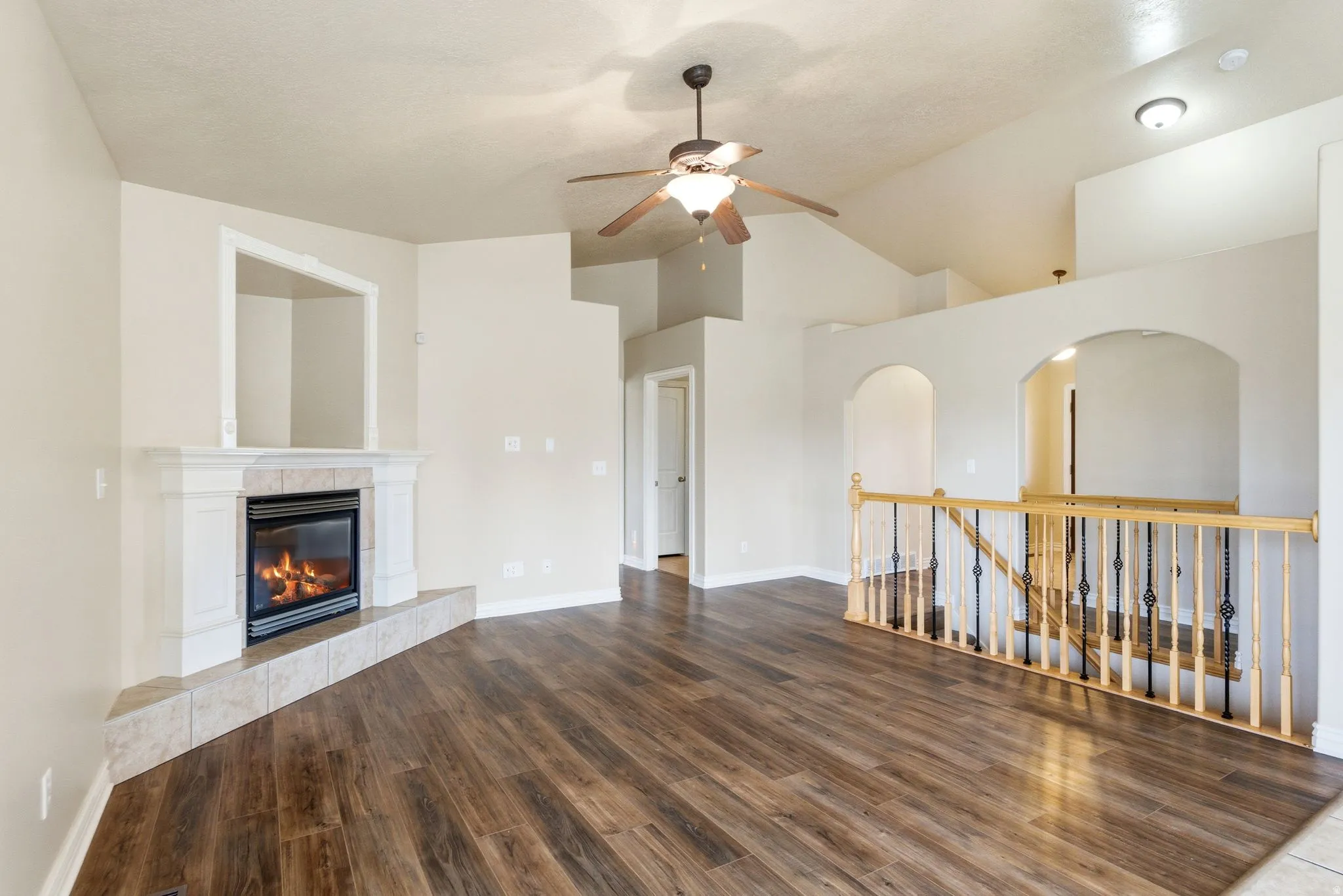 Unfurnished living room with dark wood-style floors, a tiled fireplace, lofted ceiling, and a ceiling fan