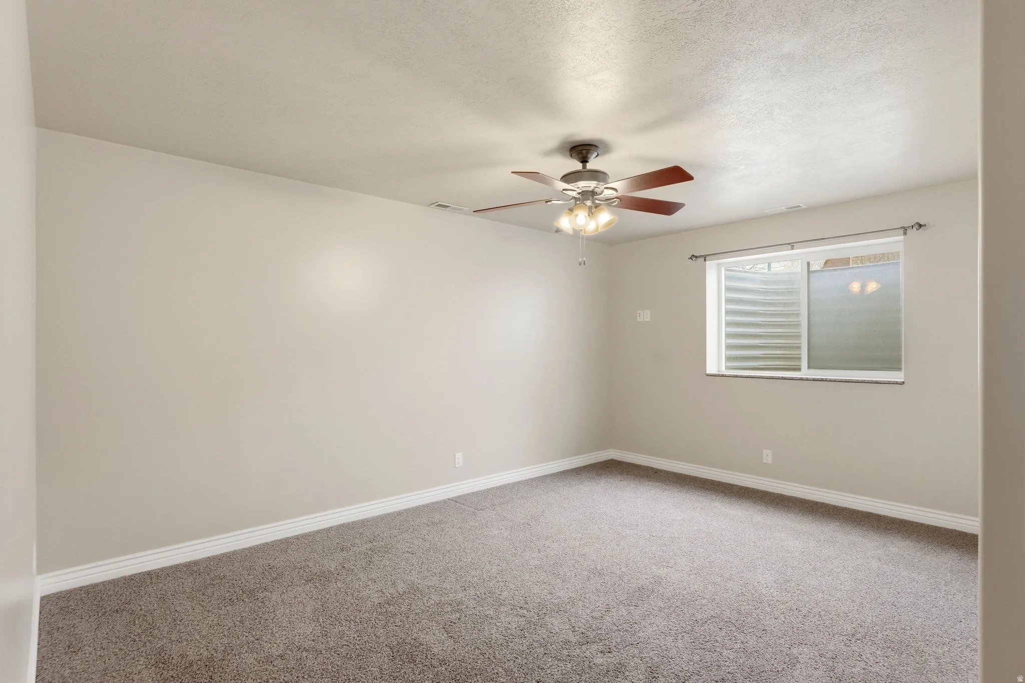 Carpeted empty room featuring a ceiling fan and a textured ceiling