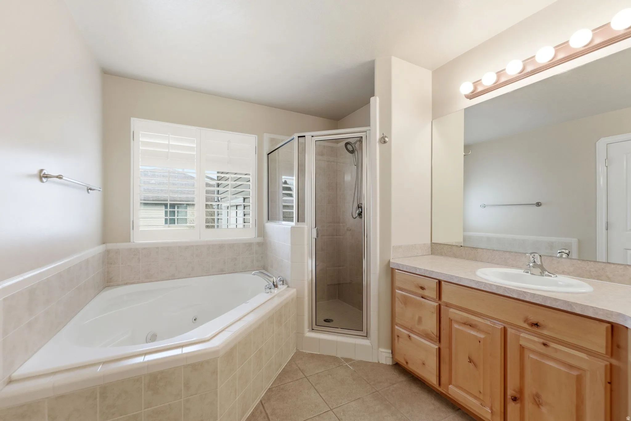 Full bath featuring vanity, a stall shower, light tile patterned floors, and a tub with jets