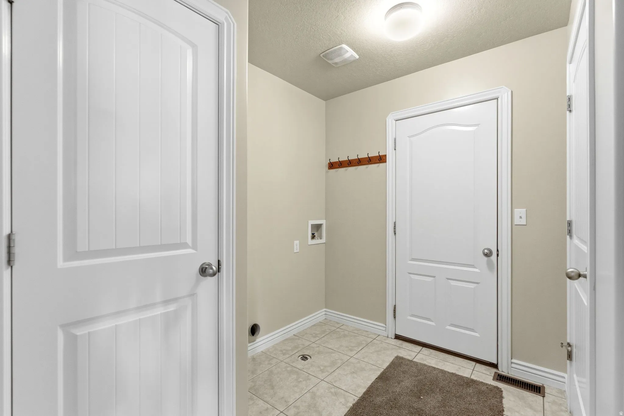 Washroom with a textured ceiling, light tile patterned floors, and washer hookup