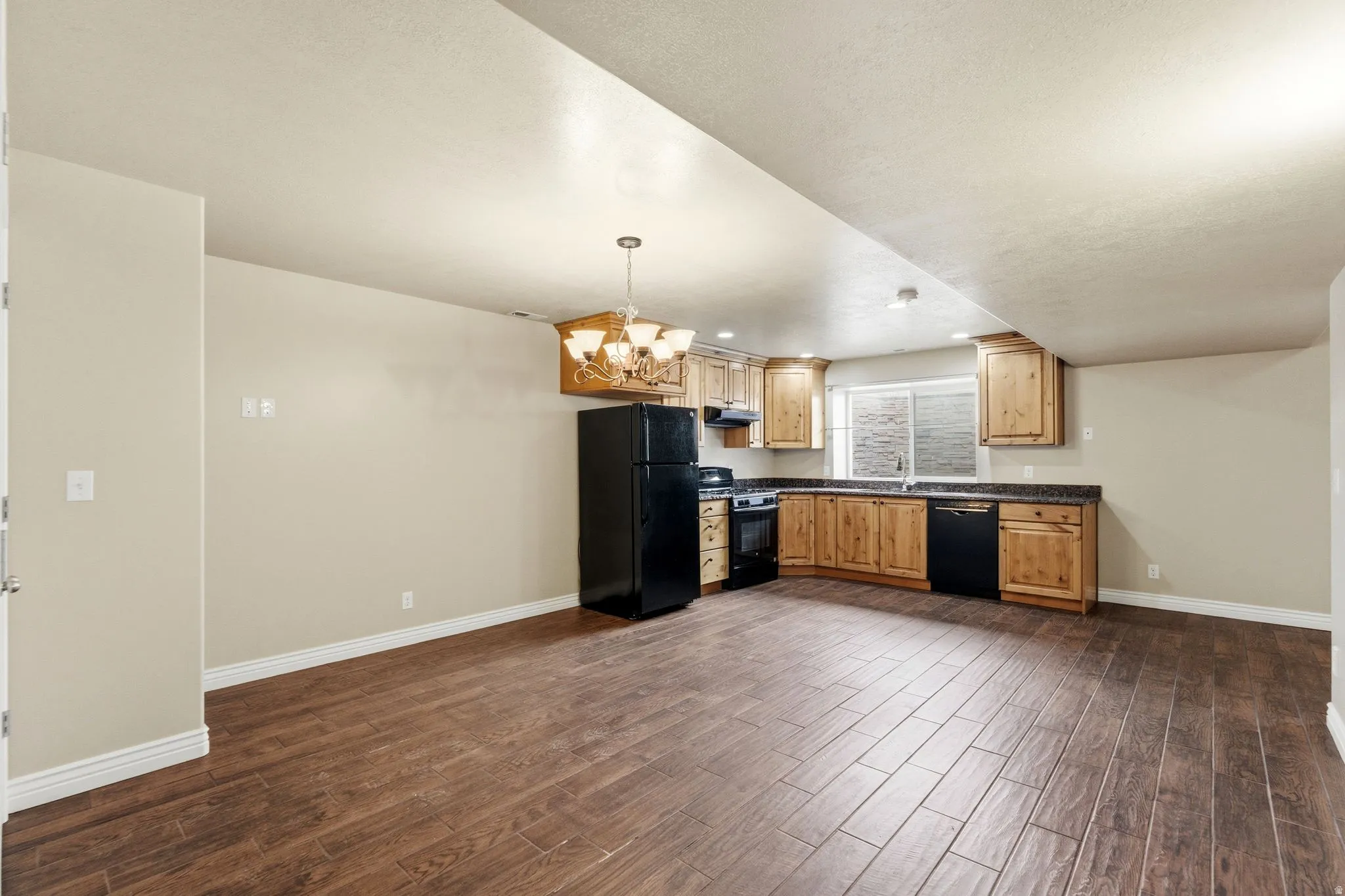 Kitchen with dark countertops, black appliances, a chandelier, and dark wood-type flooring