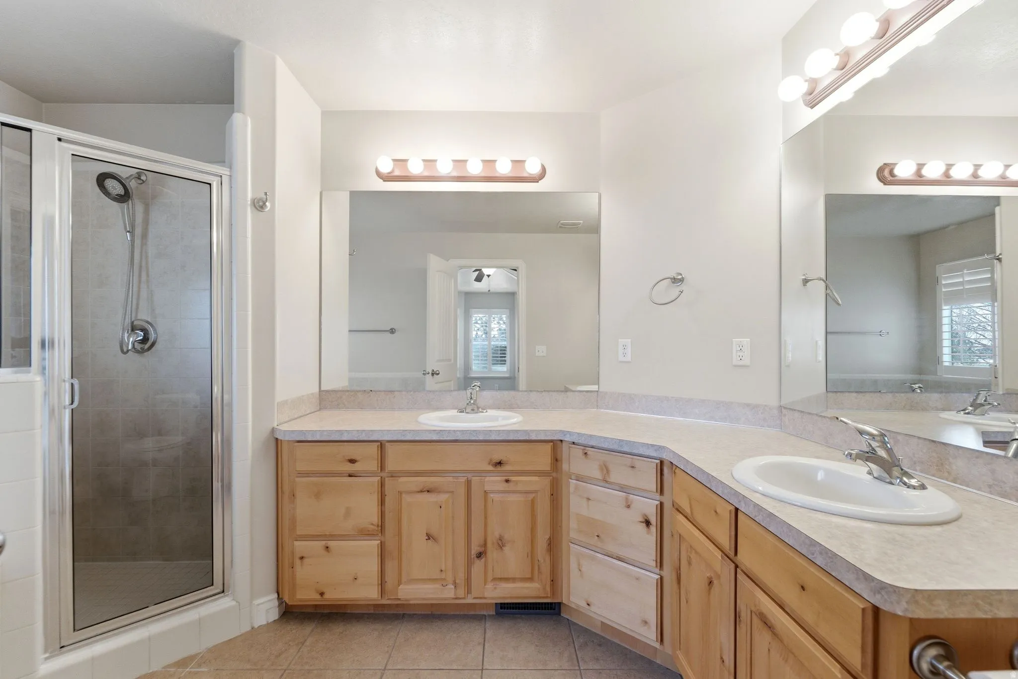 Bathroom featuring double vanity, a stall shower, light tile patterned floors, and plenty of natural light