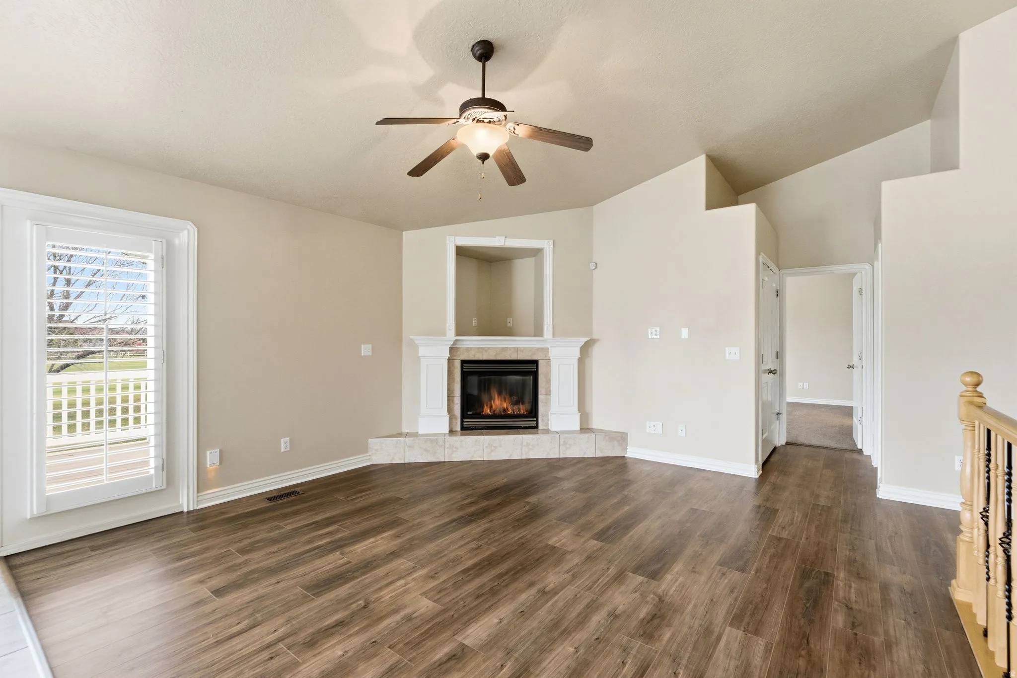 Unfurnished living room with ceiling fan, dark wood-style floors, vaulted ceiling, and a fireplace