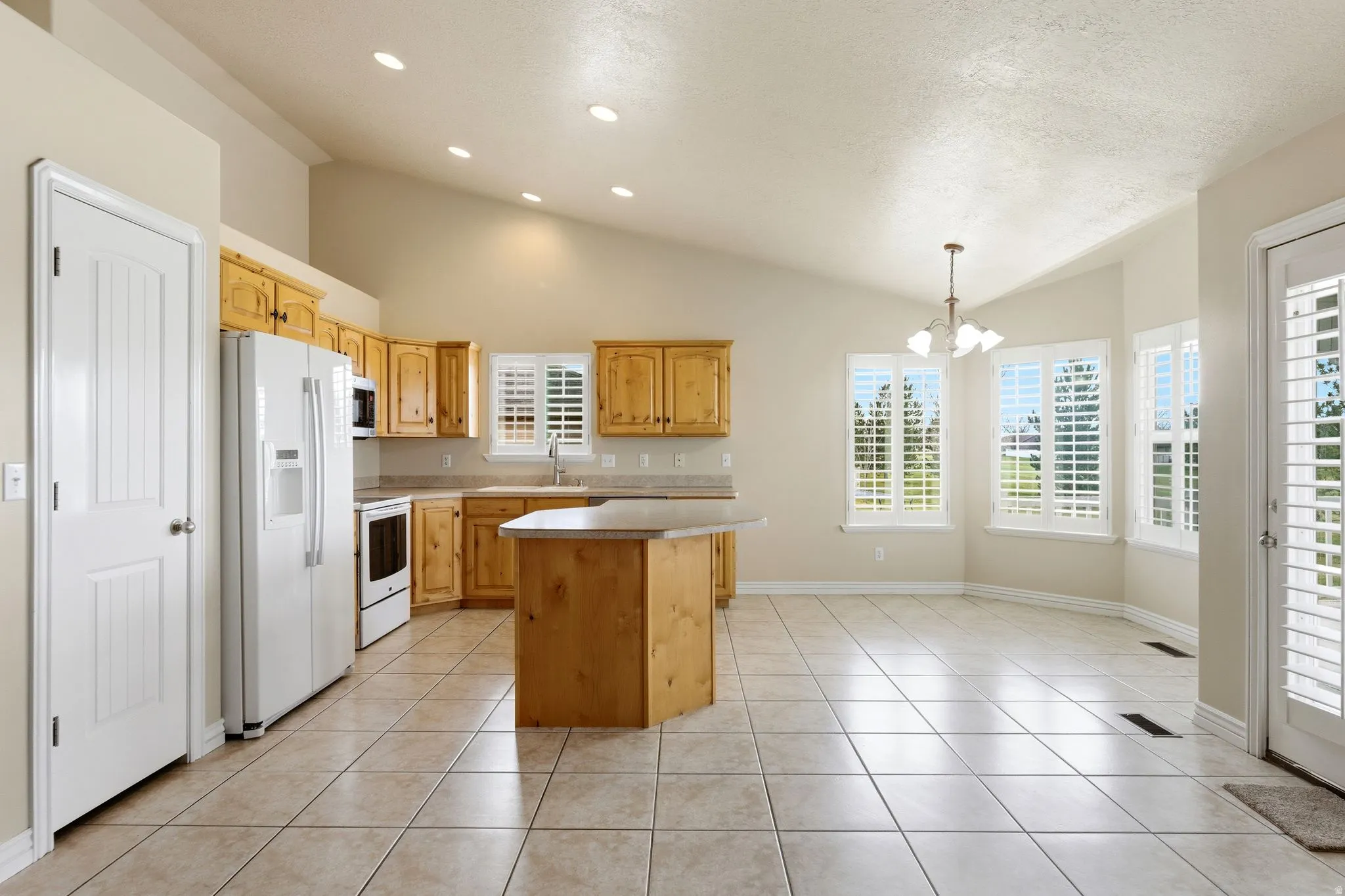 Kitchen featuring white appliances, a center island, a chandelier, light tile patterned flooring, and light countertops