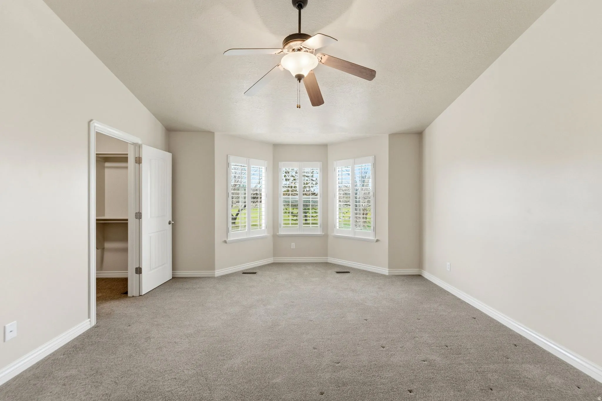 Unfurnished bedroom with a walk in closet, carpet floors, and ceiling fan