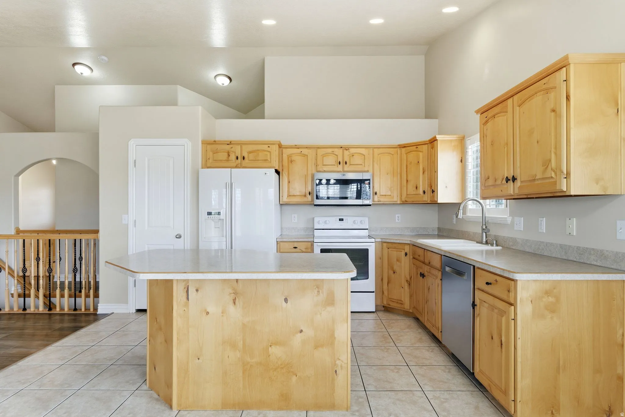 Kitchen with appliances with, light countertops, light tile patterned floors, light brown cabinets, and high vaulted ceiling