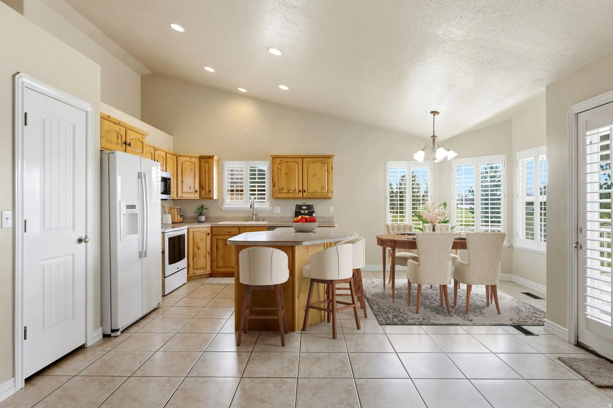 Kitchen featuring white appliances, light tile patterned flooring, a chandelier, a center island, and a textured ceiling(virtual staging)