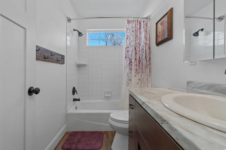 Full bath with shower / tub combo with curtain, vanity, and light wood-style floors