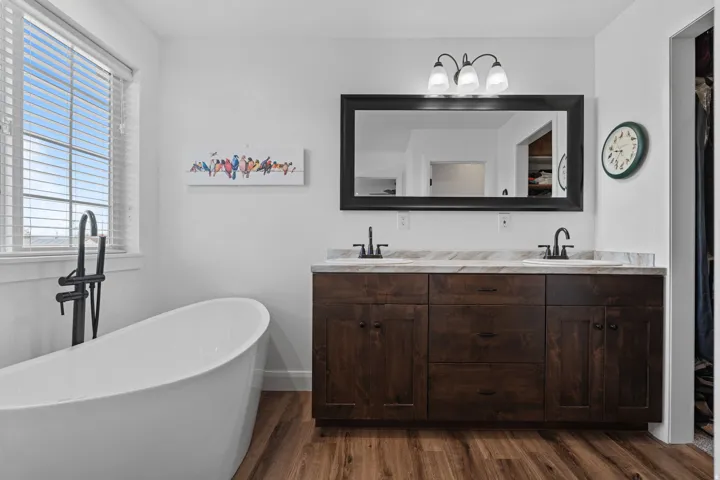 Full bath featuring double vanity, a freestanding tub, and dark wood-type flooring