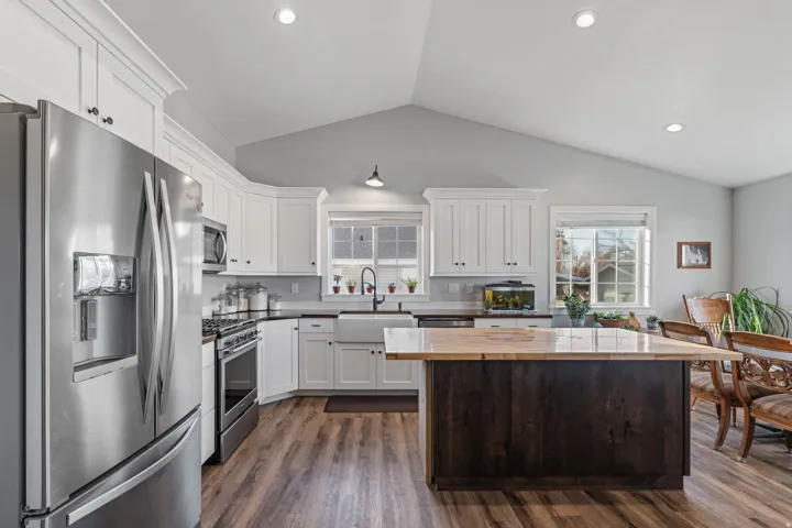 Kitchen featuring appliances with stainless steel finishes, white cabinetry, dark wood-style flooring, a center island, and lofted ceiling
