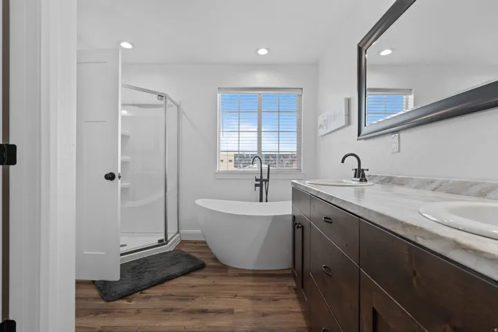 Full bath featuring double vanity, a soaking tub, dark wood-style floors, a stall shower, and recessed lighting