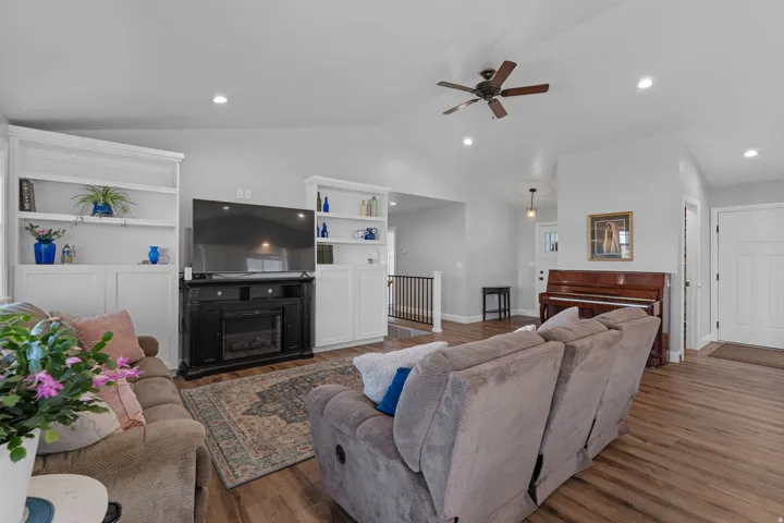 Living room with built in features, vaulted ceiling, wood finished floors, ceiling fan, and a glass covered fireplace