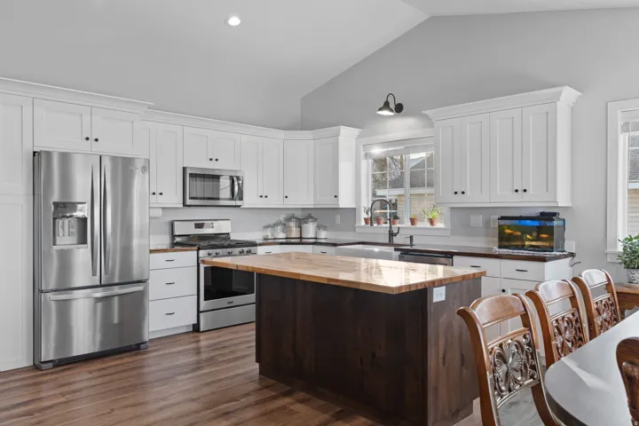 Kitchen featuring white cabinets, appliances with stainless steel finishes, butcher block counters, vaulted ceiling, and dark brown cabinets
