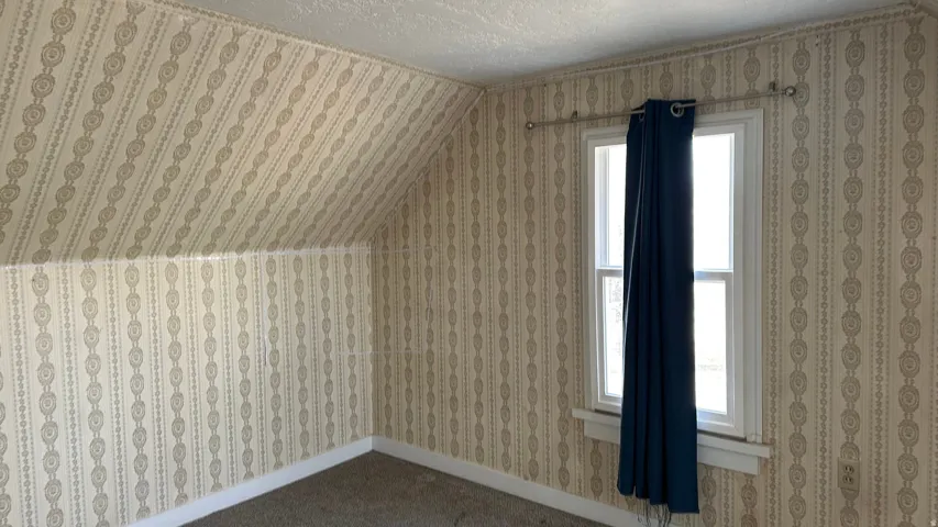 Additional living space with lofted ceiling, a textured ceiling, and wallpapered walls