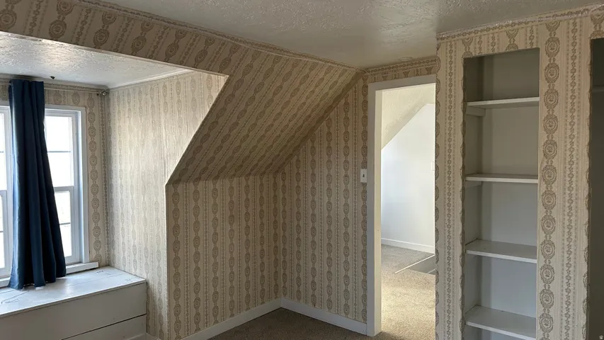 Additional living space with a textured ceiling, wallpapered walls, and carpet