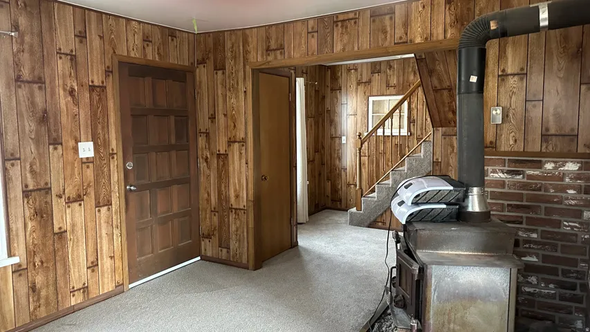 Misc room featuring a wood stove, wood walls, carpet floors, and stairway