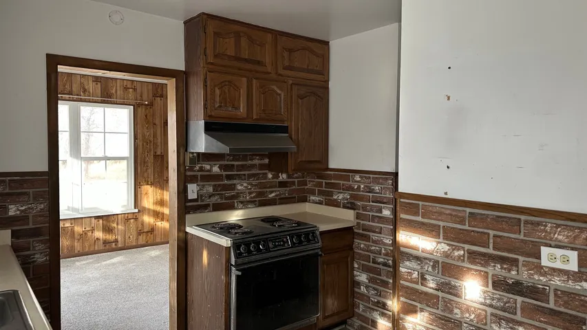 Kitchen featuring black range with electric stovetop, light colored carpet, under cabinet range hood, light countertops, and wood walls