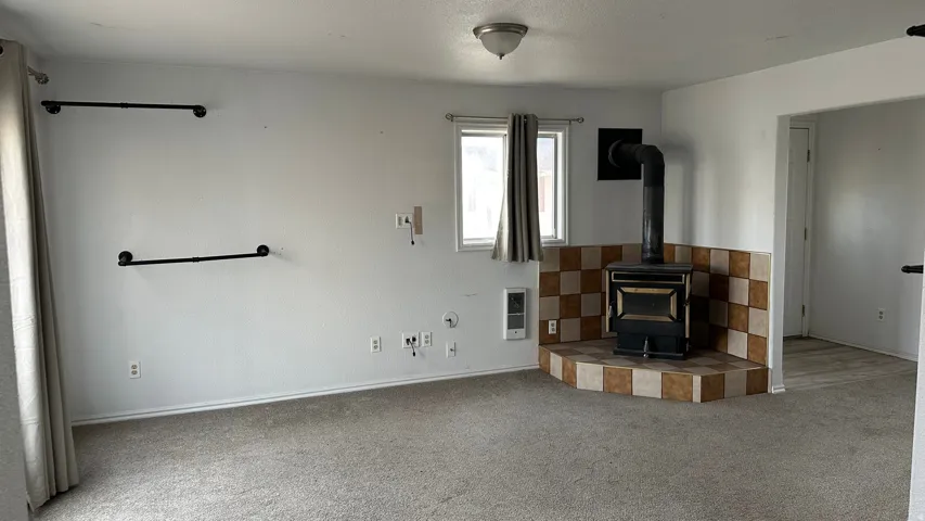 Unfurnished living room featuring a wood stove, carpet flooring, heating unit, and a textured ceiling