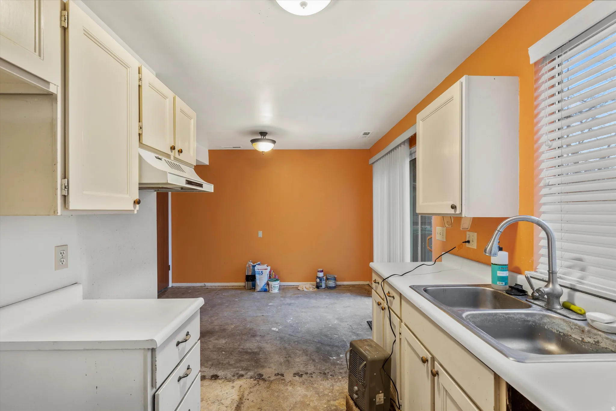 Kitchen featuring light countertops, concrete flooring, under cabinet range hood, and cream cabinetry