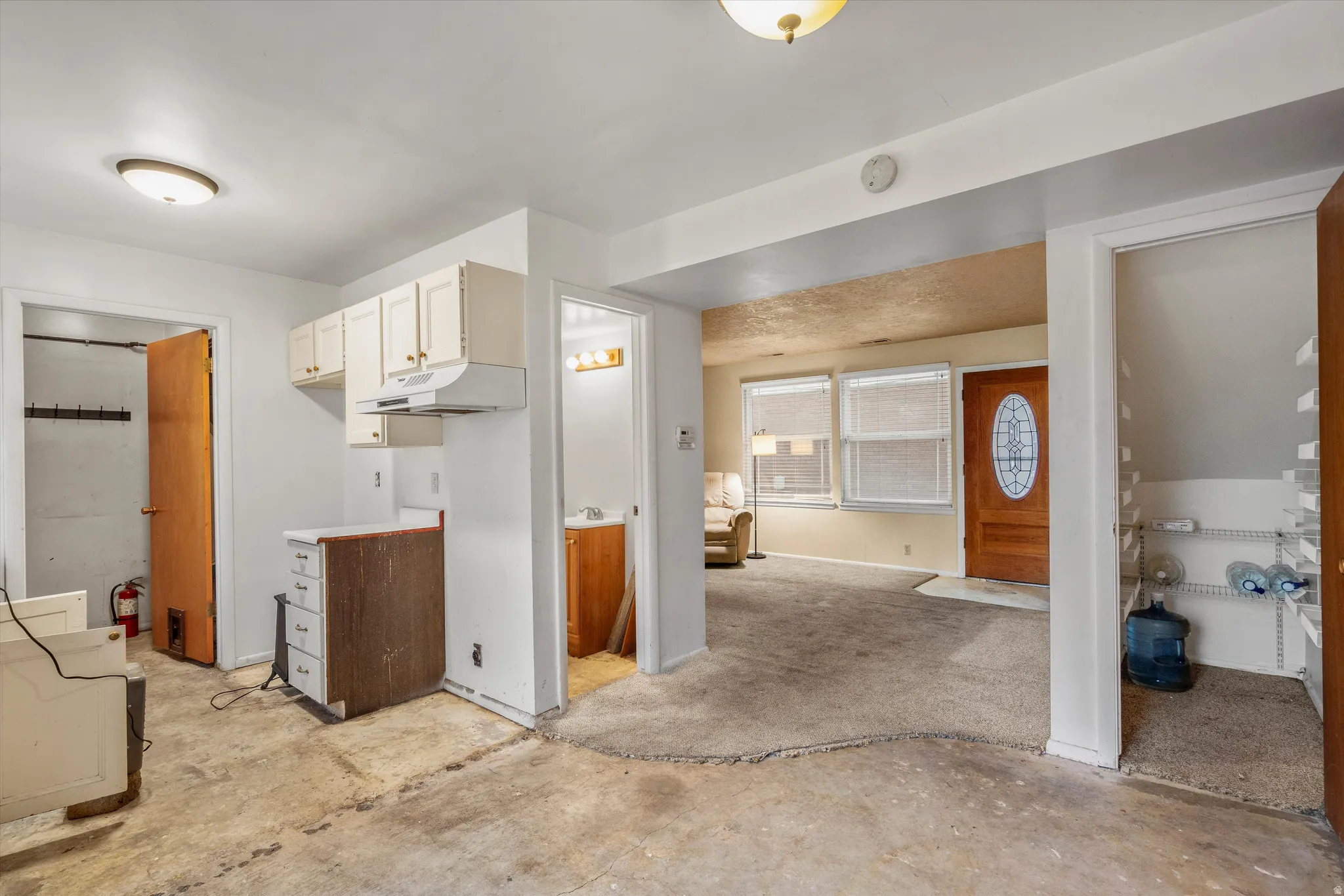 Kitchen featuring light countertops, white cabinetry, unfinished concrete floors, and under cabinet range hood