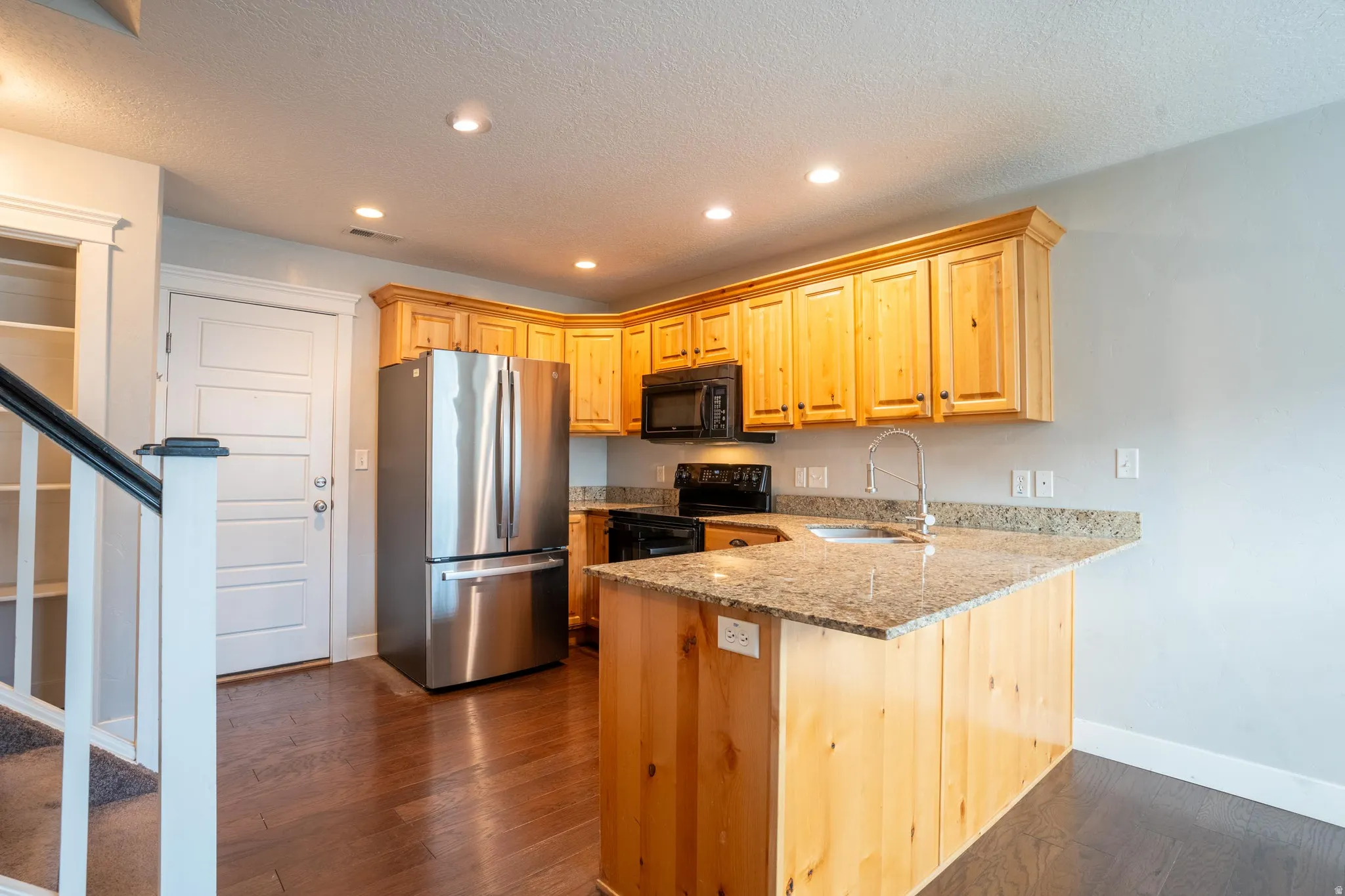 Kitchen with recessed lighting, black appliances, light stone counters, a peninsula, and dark wood finished floors
