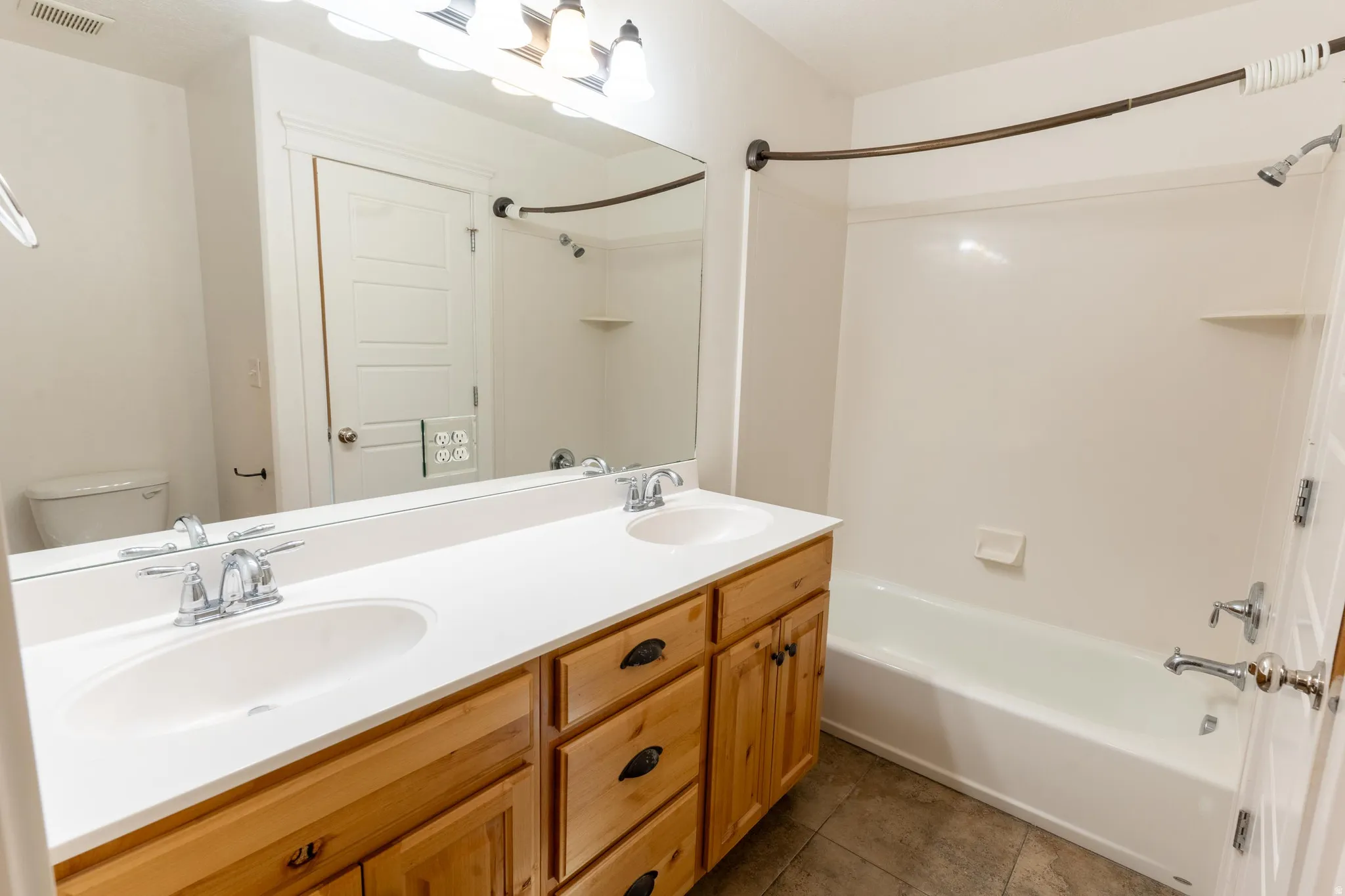 Full bathroom with shower / tub combination, double vanity, and dark tile patterned flooring adjacent to the walk-in closet
