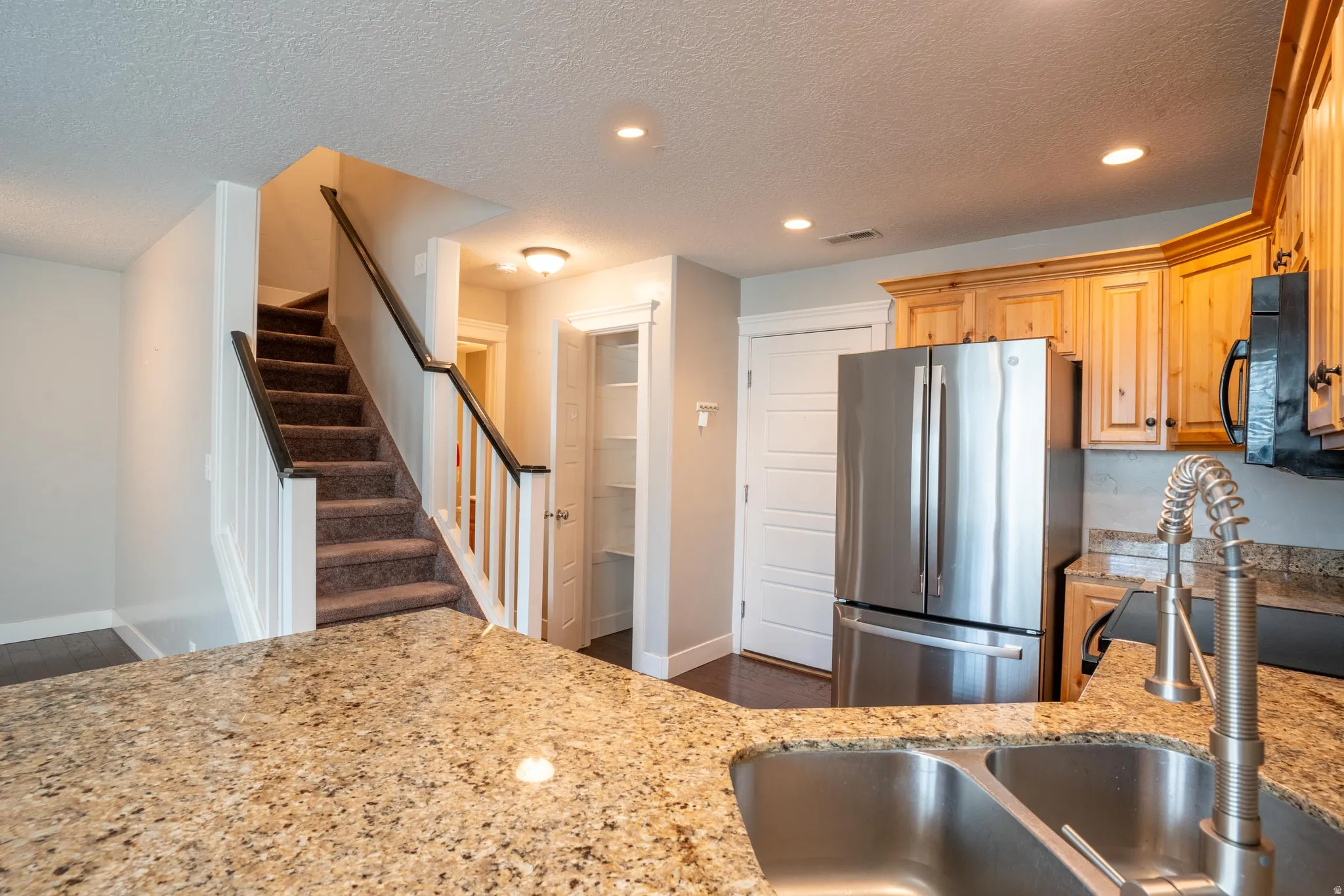 Kitchen with light stone counters, a textured ceiling, dark wood-type flooring, and recessed lighting, refrigerator is negotiable with sale of town house.