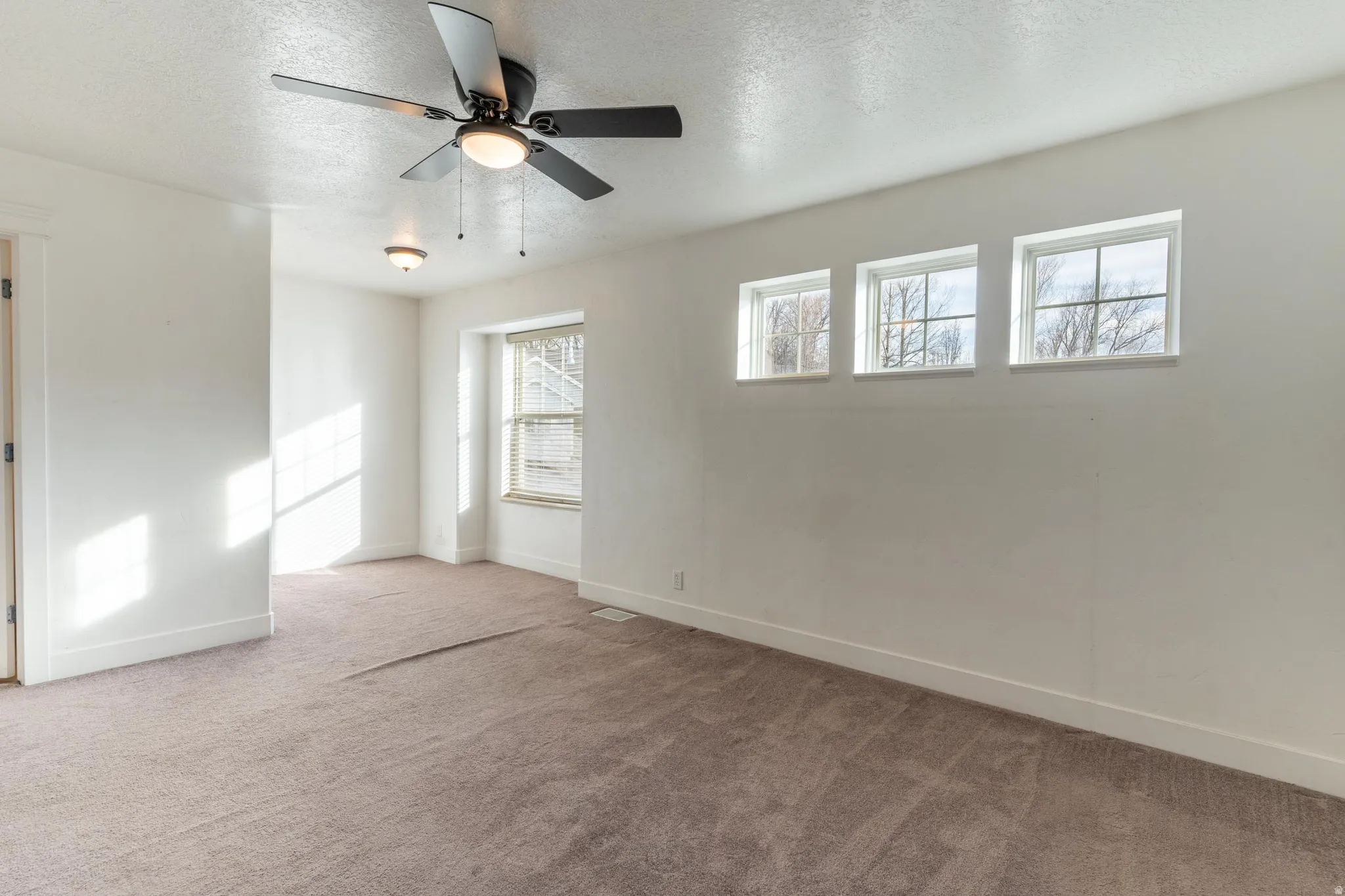 Largest primary bedroom with a textured ceiling, light colored carpet, and ceiling fan