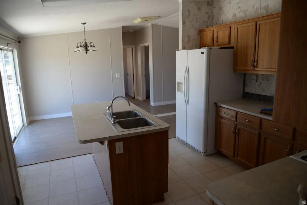 Kitchen with brown cabinets, an island with sink, hanging light fixtures, and light countertops