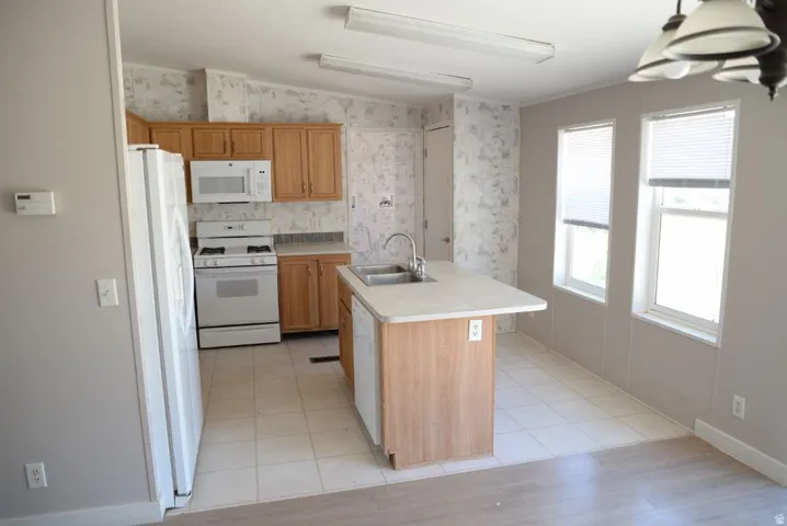 Kitchen featuring white appliances, light countertops, wallpapered walls, an island with sink, and light wood-style flooring