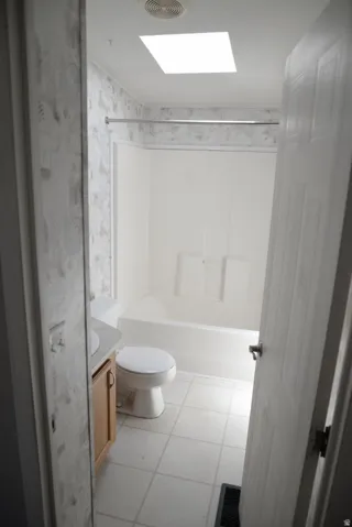 Bathroom featuring vanity, a skylight, light tile patterned floors, shower / washtub combination, and wallpapered walls