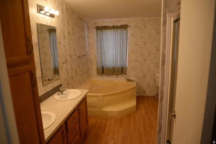 Bathroom featuring wallpapered walls, double vanity, a garden tub, light wood finished floors, and a stall shower