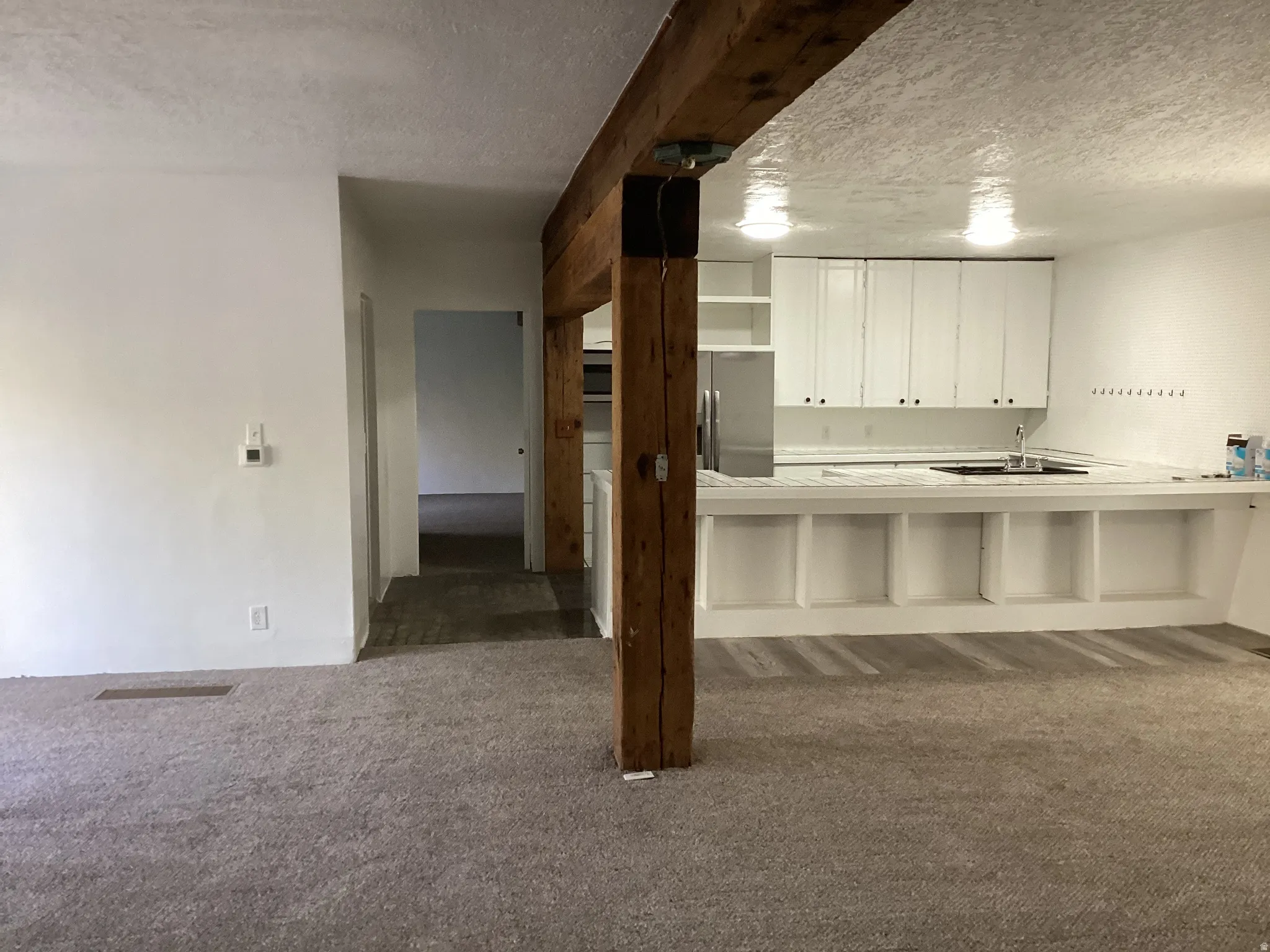 Kitchen featuring a textured ceiling, light countertops, white cabinetry, a breakfast bar, and dark colored carpet