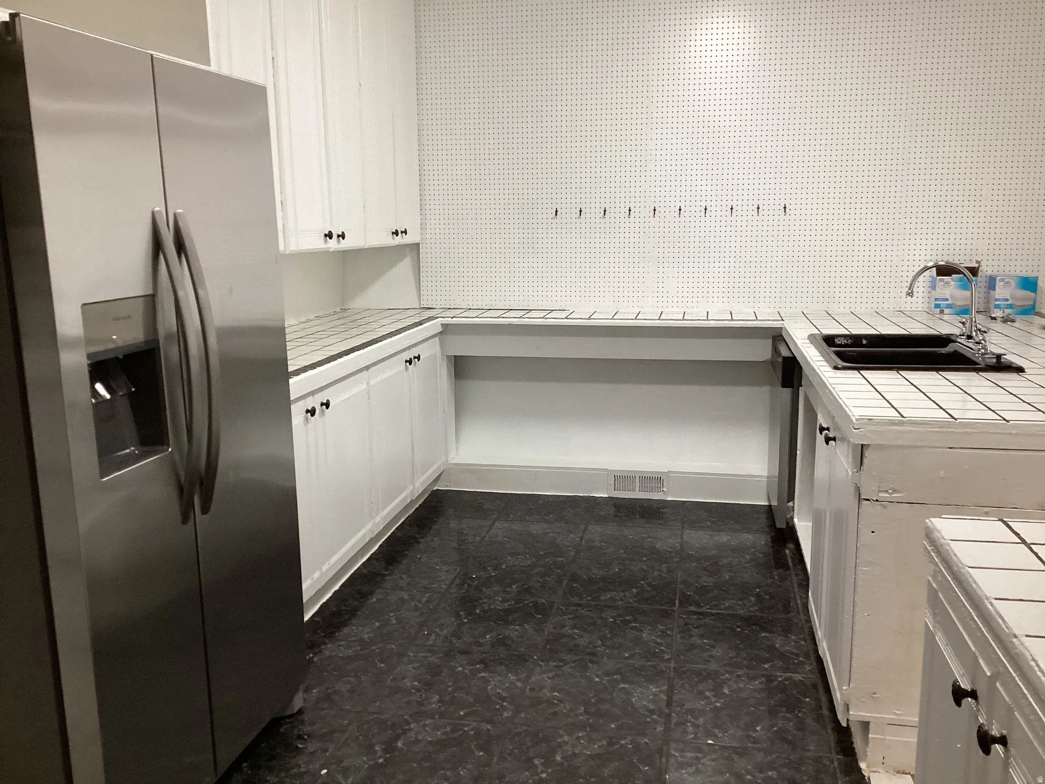 Kitchen featuring stainless steel refrigerator with ice dispenser, white cabinetry, and tile countertops
