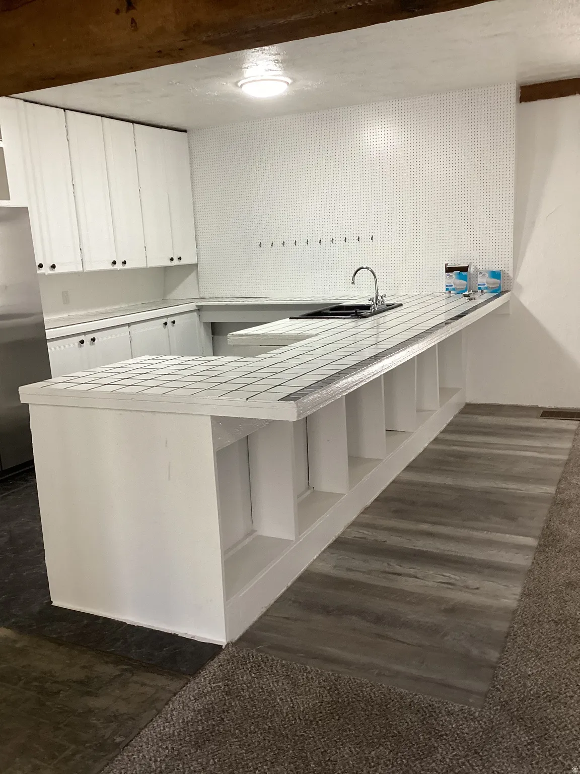 Kitchen with a peninsula, white cabinetry, stainless steel refrigerator, and a kitchen bar