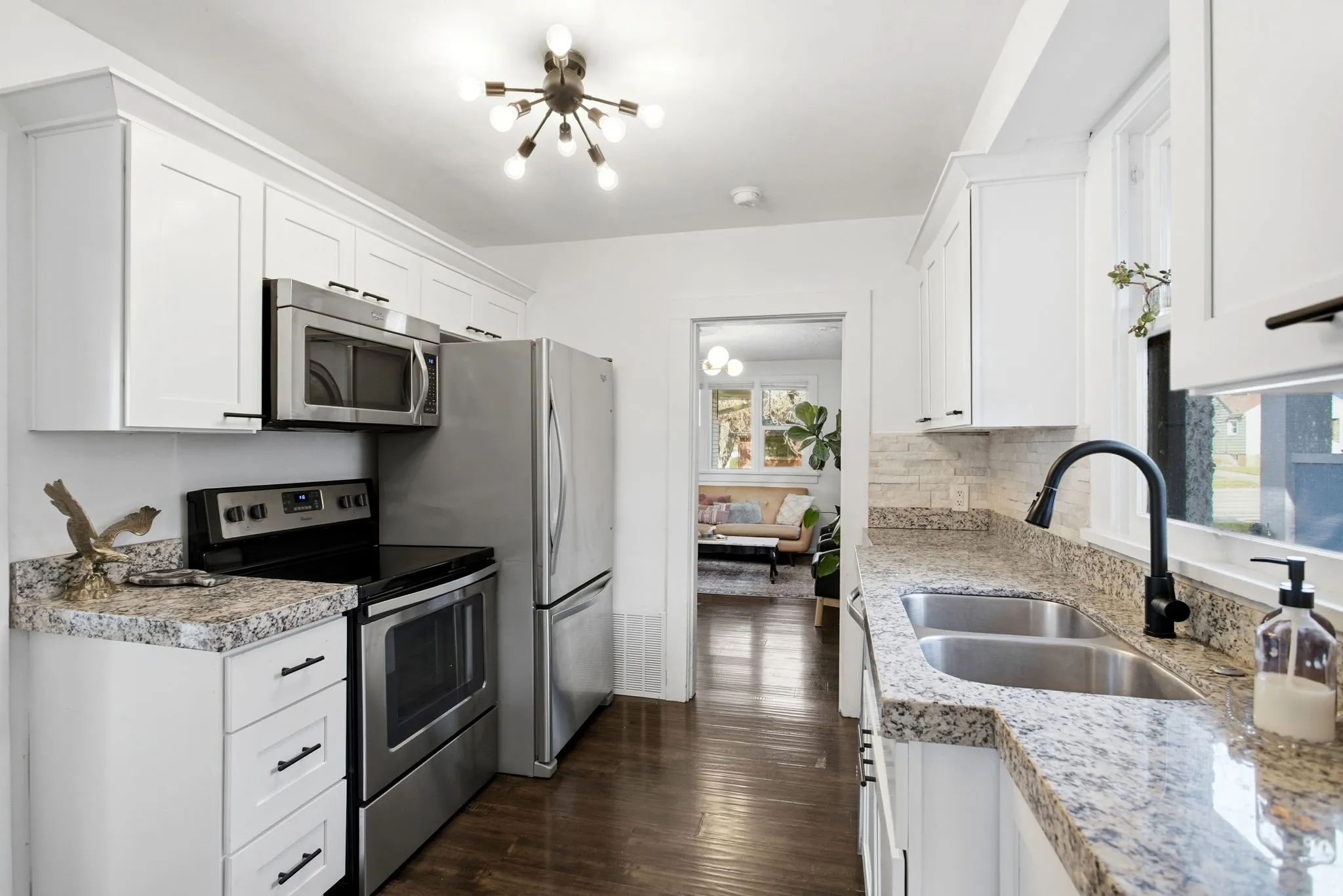 Kitchen with appliances with stainless steel finishes, dark wood-type flooring, white cabinets, and a chandelier