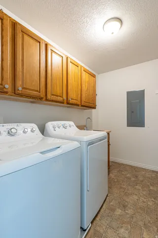 Laundry area featuring stone finish flooring, cabinet space, a textured ceiling, washer and clothes dryer, and electric panel