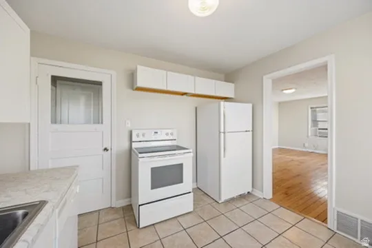 Kitchen with white cabinetry, white appliances, light countertops, and light tile patterned flooring