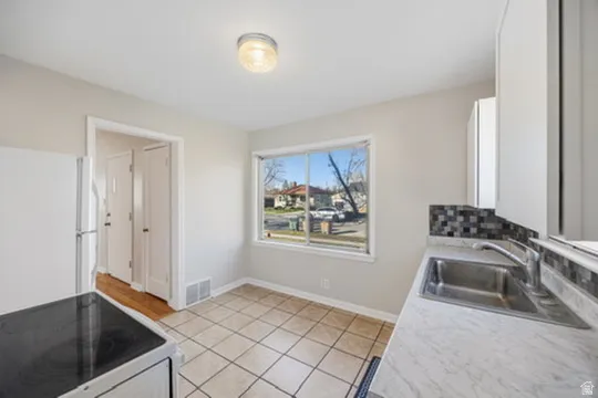 Kitchen featuring electric range oven, light countertops, freestanding refrigerator, light tile patterned floors, and white cabinetry