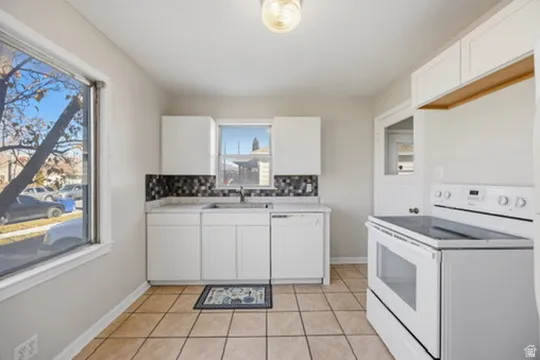 Kitchen with white appliances, white cabinetry, light tile patterned floors, light countertops, and tasteful backsplash