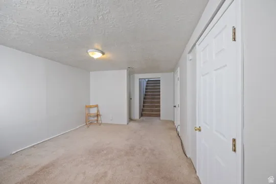 Finished below grade area with a textured ceiling, light colored carpet, and stairs