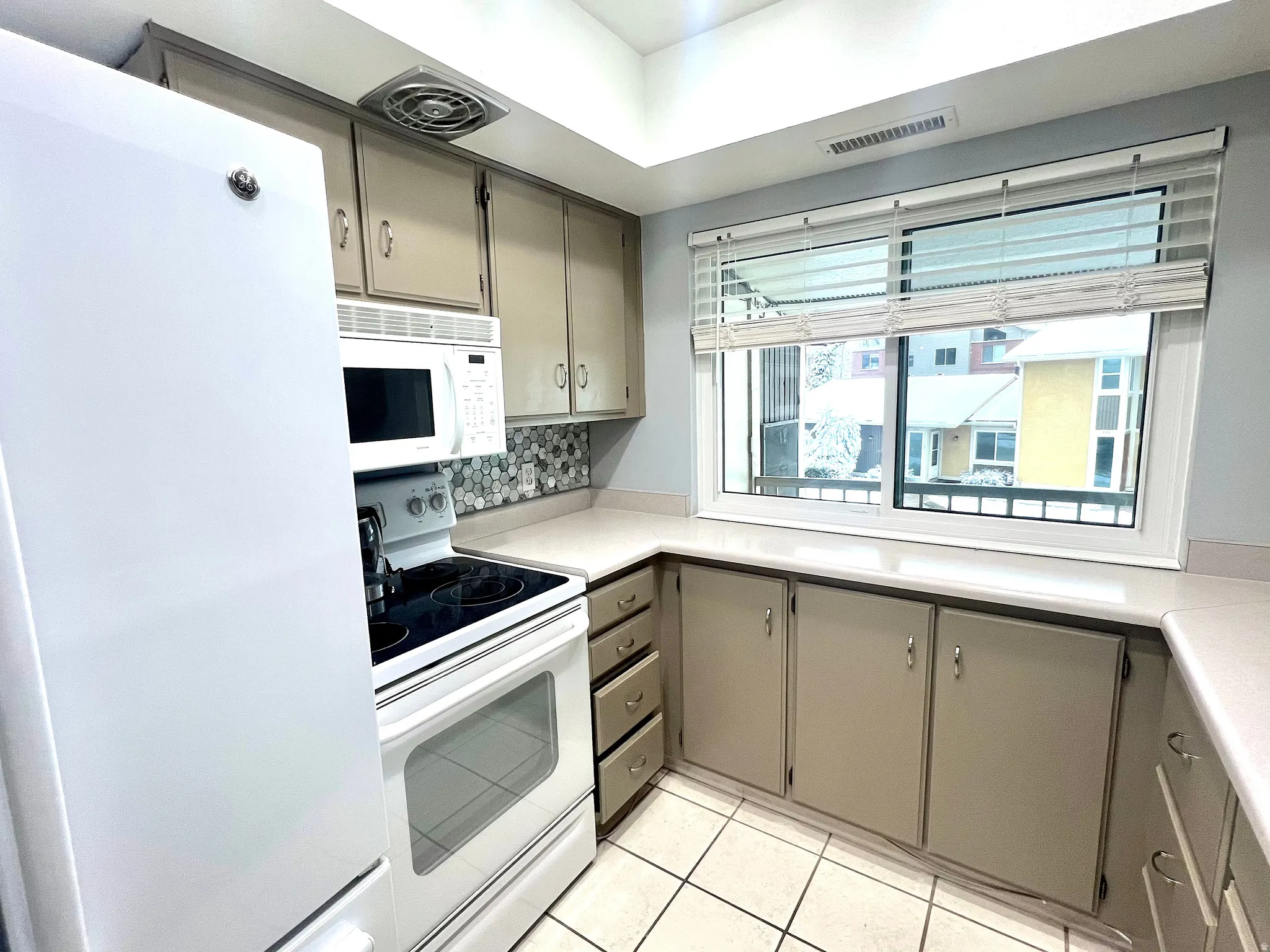 Kitchen with gray cabinetry, white appliances, light countertops, and light tile patterned floors