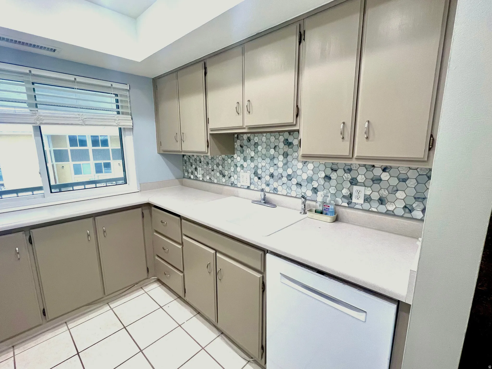 Kitchen with white dishwasher, light countertops, gray cabinets, and light tile patterned floors