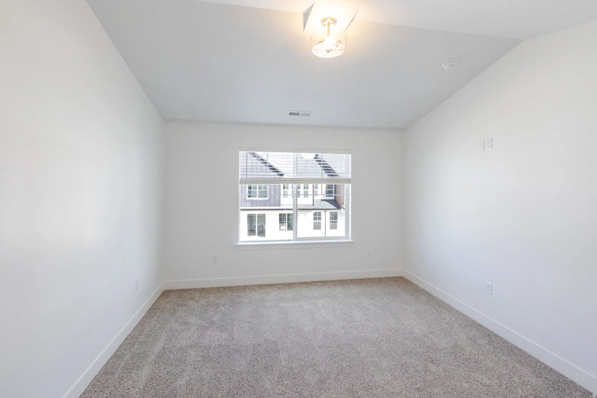 Empty room featuring light colored carpet and vaulted ceiling