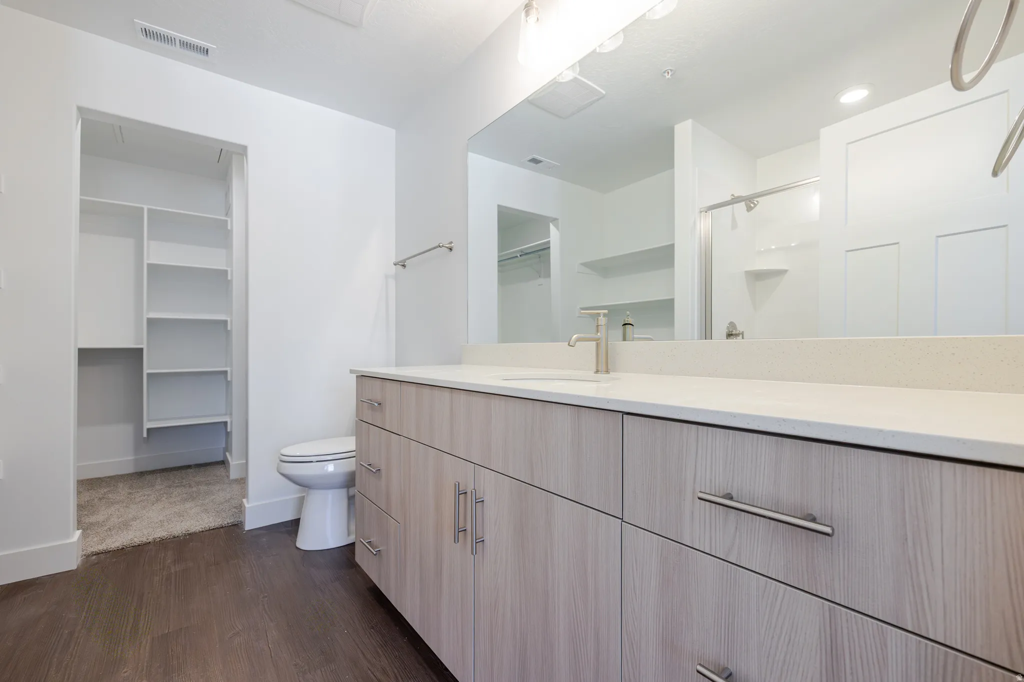 Full bathroom with a spacious closet, vanity, a shower stall, and dark wood-style flooring