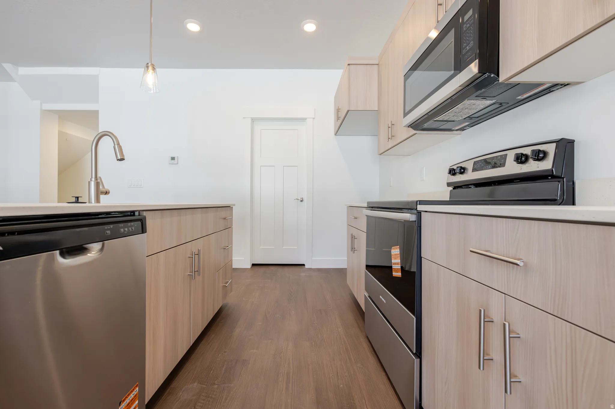 Kitchen with light wood finish cabinetry, stainless steel appliances, dark wood-type flooring, and hanging light fixtures