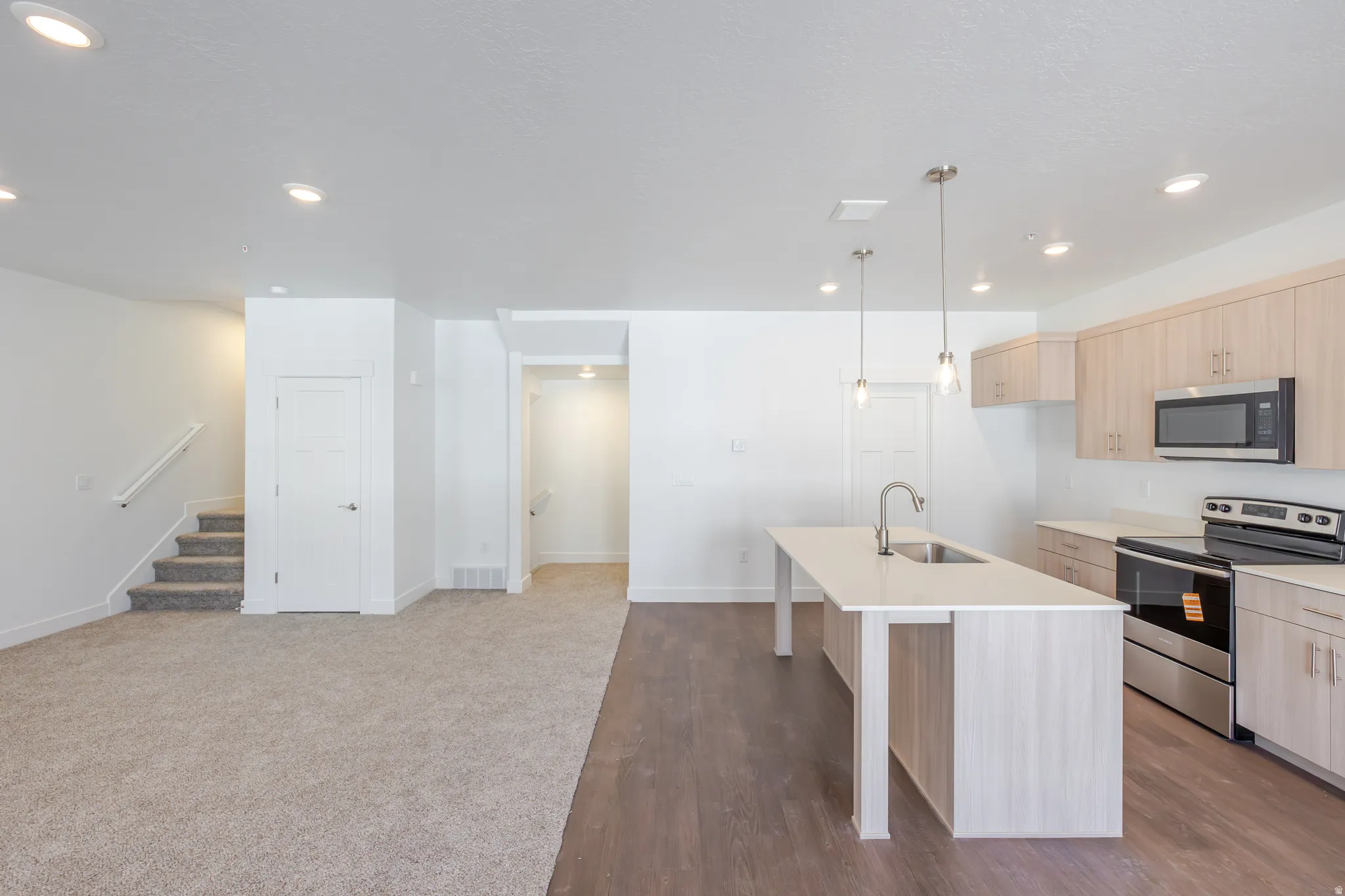 Kitchen with light wood finish cabinets, stainless steel appliances, a kitchen bar, pendant lighting, and a kitchen island with sink